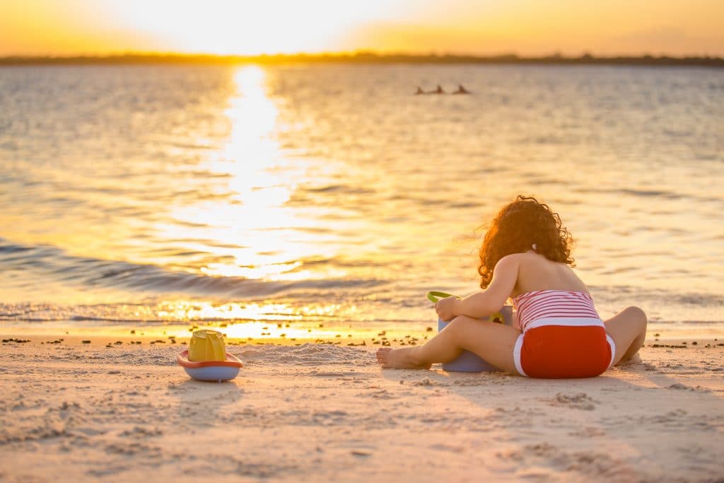 Cocoa beach family photographers photograph a portrait of a little girl playing in the sand with dolphins in the background