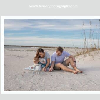 Family of 3 sitting on clearwater beach for a photography session near sand dunes