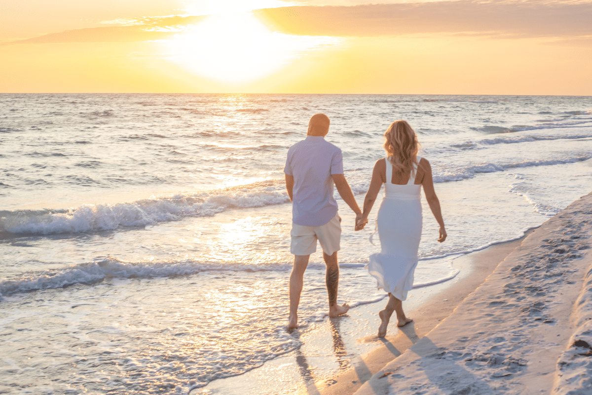 couple walking on the beach at sunset holding hands for a photography session in longboat key