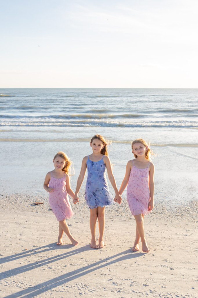 family photographers siesta key capture a portrait of sisters holding hands on the beach