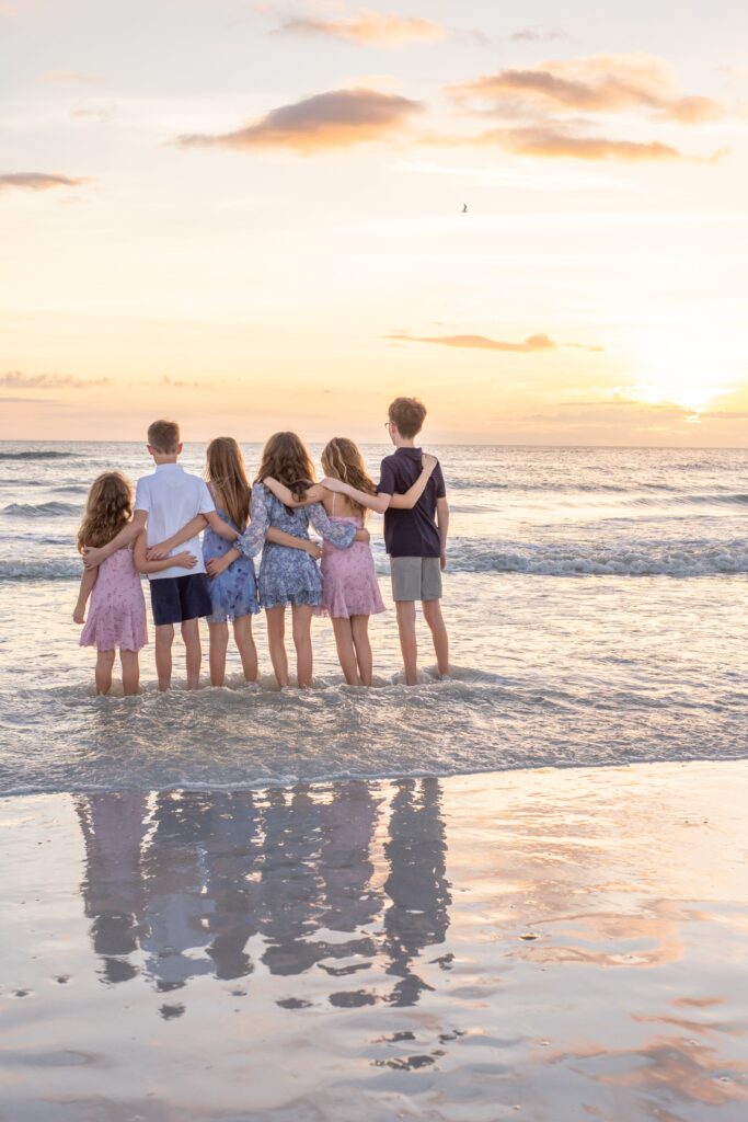 siesta key beach photographer captures a photo of cousins with their arms around each other I the water looking at the sunset